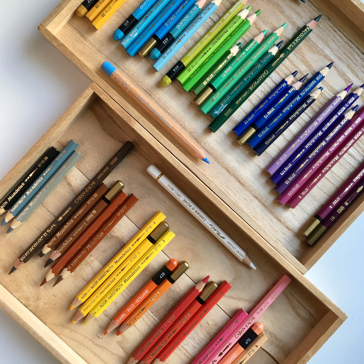 An open wooden box filled with SupraColor pencils by Caran d'Ache, neatly sorted by hues.